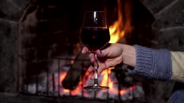 Una copa de vino en una mano de mujer sobre el fondo del fuego en la chimenea — Vídeos de Stock