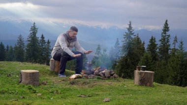 Dağlarda ateşin yanında bir adam