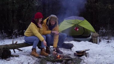 Genç bir adam ve kadın kış ormanında piknik yapıyorlar.