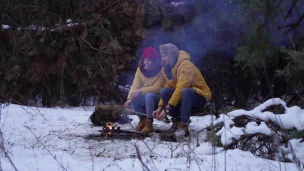 Junge Männer und Frauen im Winter am Lagerfeuer im Wald — Stockvideo