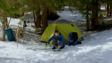 Kadın kış ormanında çadırın yanında yemek hazırlıyor.