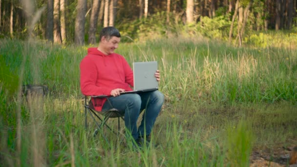 Gal programmerer som jobber med laptop i sommerskog – stockvideo