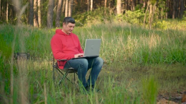 Człowiek pracujący na laptopie w letnim lesie — Wideo stockowe