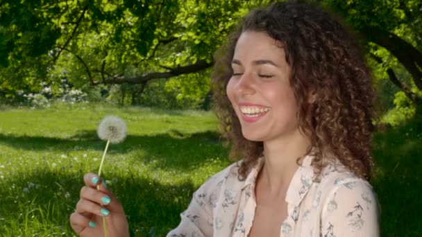 Jong meisje portret blaast paardenbloem blaas bal bloem in een lente park — Stockvideo