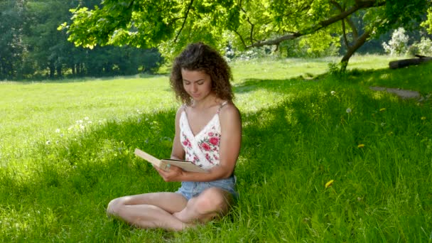 Étudiante lit un livre sur la pelouse dans le parc — Video
