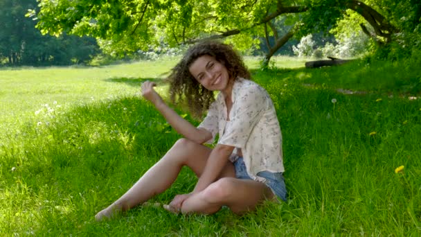 Gelukkig meisje zit op het gras in het park — Stockvideo
