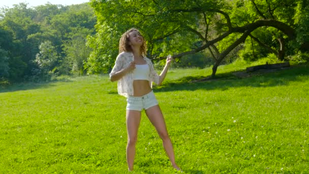 Een jonge mooie vrouw dansend op het gras in het park — Stockvideo