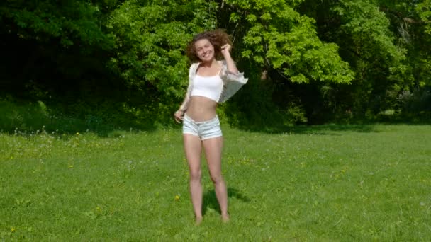 Een jonge mooie vrouw dansend op het gras in het park — Stockvideo