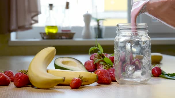 Batido de plátano fresa se vierte en un vaso sobre el fondo de frutas frescas — Vídeos de Stock