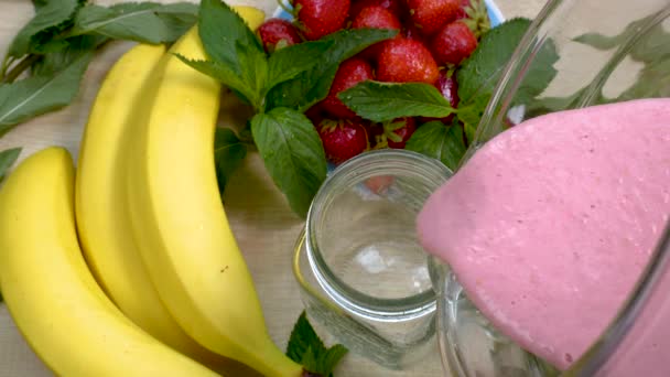 Strawberry Banana Smoothie dituangkan ke dalam gelas di latar belakang buah-buahan segar — Stok Video