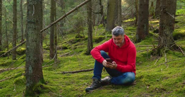 Бородатый мужчина с телефоном в лесу — стоковое видео