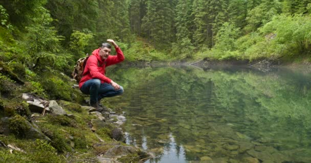 Szakállas férfi hátizsákkal közel a tiszta hegyi tó — Stock videók