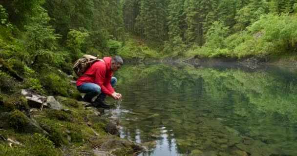 Egy szakállas férfi hátizsákkal lemossa magát vízzel egy tiszta tóból. — Stock videók