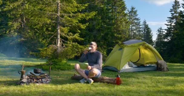 El hombre bebe té y mira el mapa en el Camping. — Vídeos de Stock