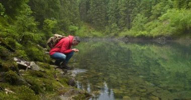 Sırt çantalı sakallı bir adam temiz bir gölden su içer.