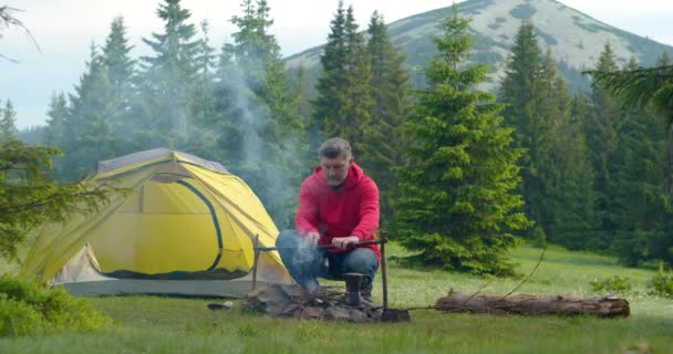 Бородач готовит пищу на костре в горах. — стоковое видео