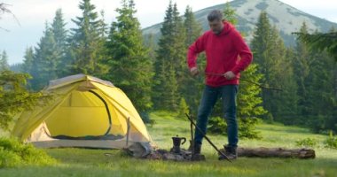 Sakallı bir adam dağlardaki güzel bir orman çimenliğinde ateş yakar.