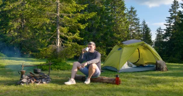 A bearded man is drinking tea near the fire — Stock Video