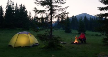 Sakallı erkek turist, ellerini dağlardaki şenlik ateşinde ısıtıyor.