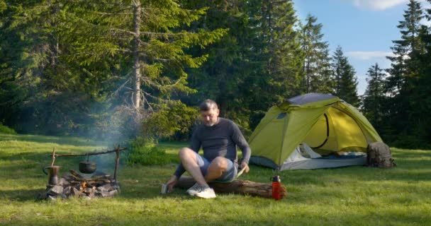 De man drinkt thee en kijkt naar de kaart op de camping. — Stockvideo