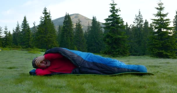 Bearded man sover i en sovsäck på en vacker äng i bergen — Stockvideo