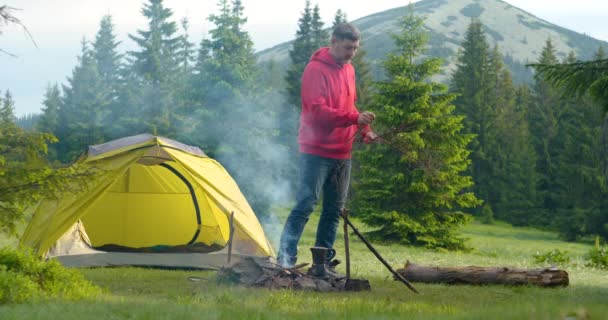 Un hombre barbudo enciende un fuego en un hermoso césped forestal en las montañas — Vídeos de Stock