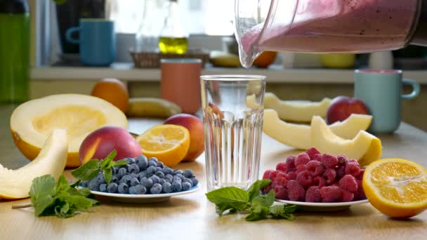 Raspberry Blueberry Melon Smoothie dituangkan ke dalam gelas di latar belakang buah-buahan segar — Stok Video