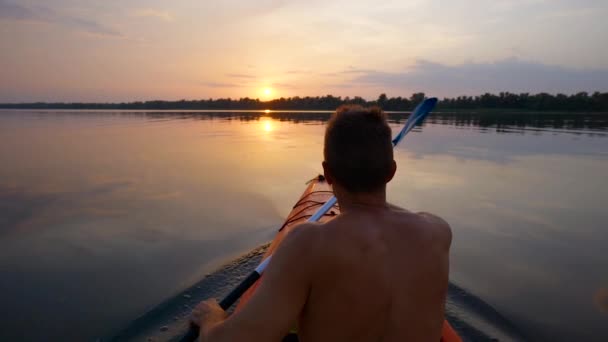 Un hombre kayaks en un río tranquilo hacia el atardecer — Vídeos de Stock