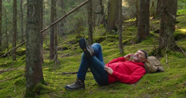 Un homme barbu se repose et parle au téléphone dans la forêt — Video
