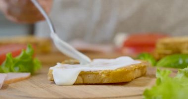 Evin mutfağındaki kadın aşçı sandviç topluyor.