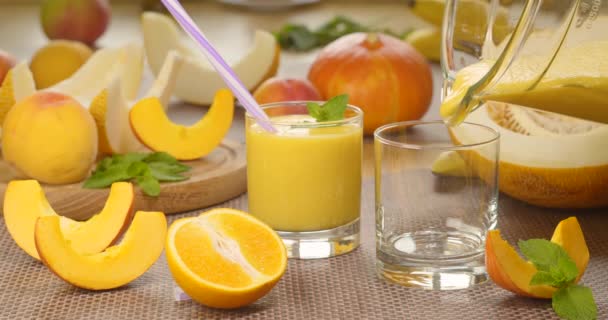 Melone Banana Orange Smoothie wird in ein Glas auf dem Hintergrund frischer Früchte gegossen — Stockvideo