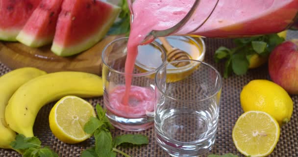 Watermeloen banaan sinaasappel Smoothie wordt gegoten in een glas op de achtergrond van vers fruit — Stockvideo