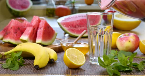 Vattenmelon banan apelsin Smoothie hälls i ett glas på bakgrunden av färska frukter — Stockvideo