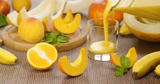 Melone Banana Orange Smoothie wird in ein Glas auf dem Hintergrund frischer Früchte gegossen — Stockvideo