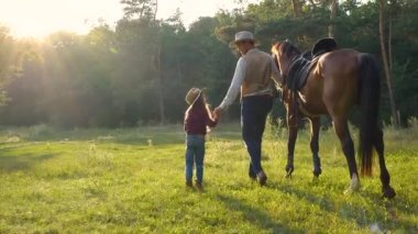 Atlı bir kovboy ve güzel kızı otlakta yürüyorlar.