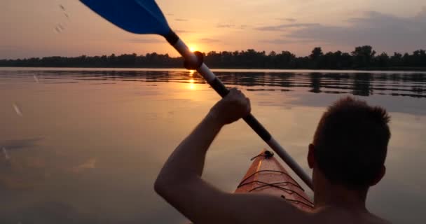 男が夕日に向かって穏やかな川でカヤックをしている — ストック動画