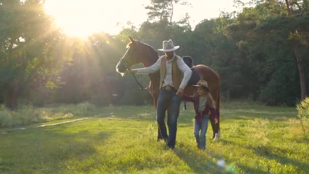 Un vaquero con un caballo y su hermosa hija están caminando en el pasto — Vídeo de stock
