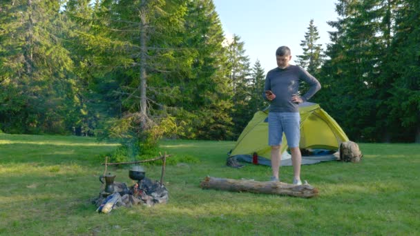 Homem barbudo perto de fogueira e tenda nas montanhas — Vídeo de Stock
