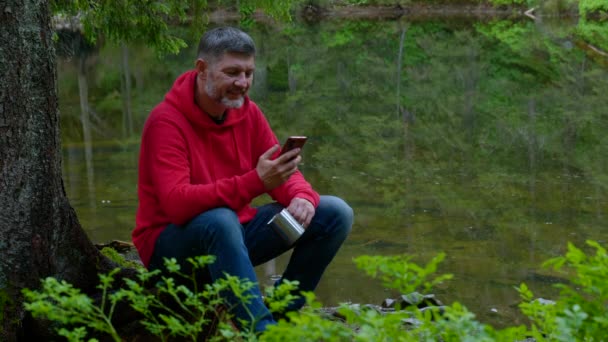 Bärtiger Mann mit Handy in der Nähe eines Bergsees — Stockvideo