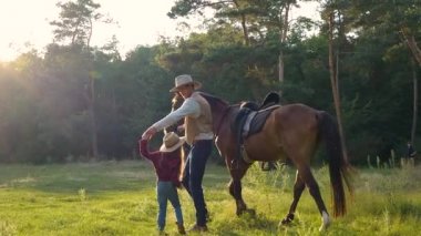 Atlı bir kovboy ve güzel kızı otlakta yürüyorlar.