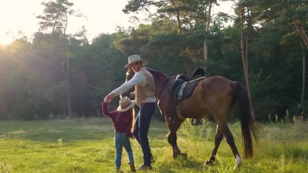 Egy cowboy egy lóval és gyönyörű lányával sétál a legelőn. — Stock videók