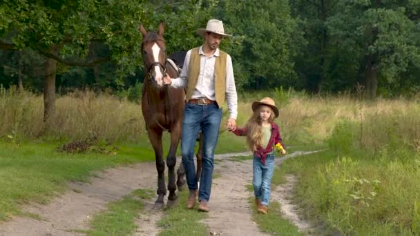 Cowboy avec sa fille marchant avec un cheval sur une route forestière — Video