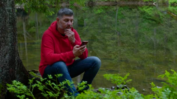 Vousatý muž s telefonem u horského jezera — Stock video