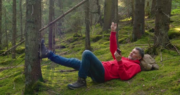 Telefonlu turist ormandaki yosunların üzerinde dinleniyor. — Stok video