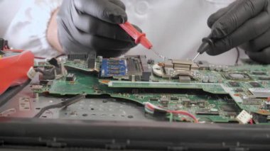 Elektronik bileşenleri hassas aletlerle test eden teknisyen, siyah eldivenli ellerin yakın görüntüsü anakart üzerindeki mikroçip performansını kontrol etmek için sondalar kullanıyor.