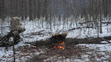 Bir adam karla kaplı bir ormanda yakacak odun topluyor ve soğuk havadan korunmak için bir barınak inşa etmeye hazırlanıyor.