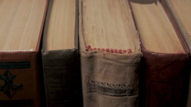 Görünür sayfa kenarları ile dikey olarak sıralanmış eski ciltli kitapların kapatılması, kağıt kenarları, ciltler ve yıpranmış yüzeyler gösteren eski cilt kapağı kitapları