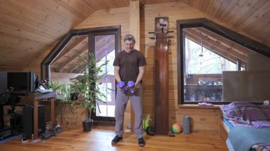 Orta yaşlı bir adam ahşap odada halter egzersizi yapıyor, yetişkin erkek antrenmanı evde profesyonel ekipman olmadan.