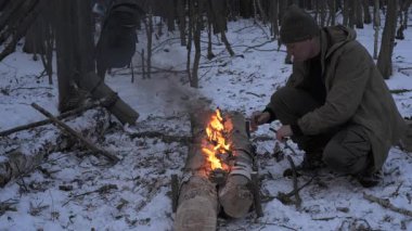Bushcraft adamı kış orman hayatta kalma kampında uzun ateş odunlarını korurken, yetişkin erkek, soğuk mevsim çalı çırpı faaliyetleri sırasında ahşap odunlarda yangını kontrol ediyordu.