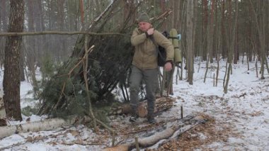 İlkel bir barınağın yanına inşa ettiği çalı turisti. Soğuk mevsimlerde yapılan yürüyüşler sırasında hayatta kalmak için ağaçlardan yapılmış bir barınak..